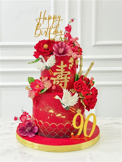 Kue ulang tahun ke-90 berwarna merah dengan bunga dan detail emas