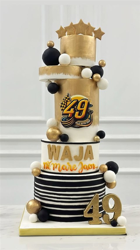 Kue bertingkat putih, hitam, dan emas dengan logo Waja Motor Group 49 serta bintang emas