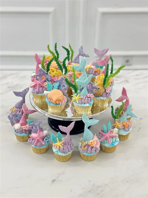 Set cupcake dalam cup emas dengan ekor mermaid pastel, kerang, bintang laut dan karang di atas penyangga bundar