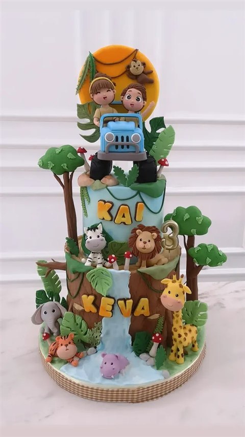 Kue jungle bertingkat dengan jeep biru, singa, zebra, jerapah, dan air terjun.