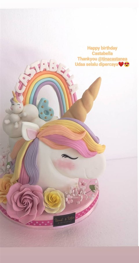 Kue unicorn putih dengan surai pastel, tanduk emas, pelangi, bunga dan angka enam