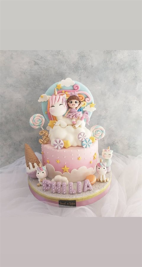 Kue unicorn pink bertuliskan Philia dengan figur anak, lolipop pastel, awan dan bintang
