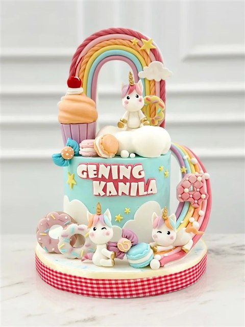 Kue turquoise Geving Kanila dengan tiga unicorn putih, pelangi dan dekorasi manis pastel