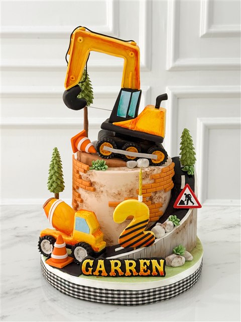 Kue Garren dengan ekskavator oranye, truk proyek, jalan berliku, dan angka dua