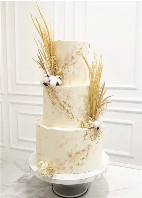 Kue wedding tiga tingkat ivory dengan dekorasi botanikal keemasan dan aksen putih